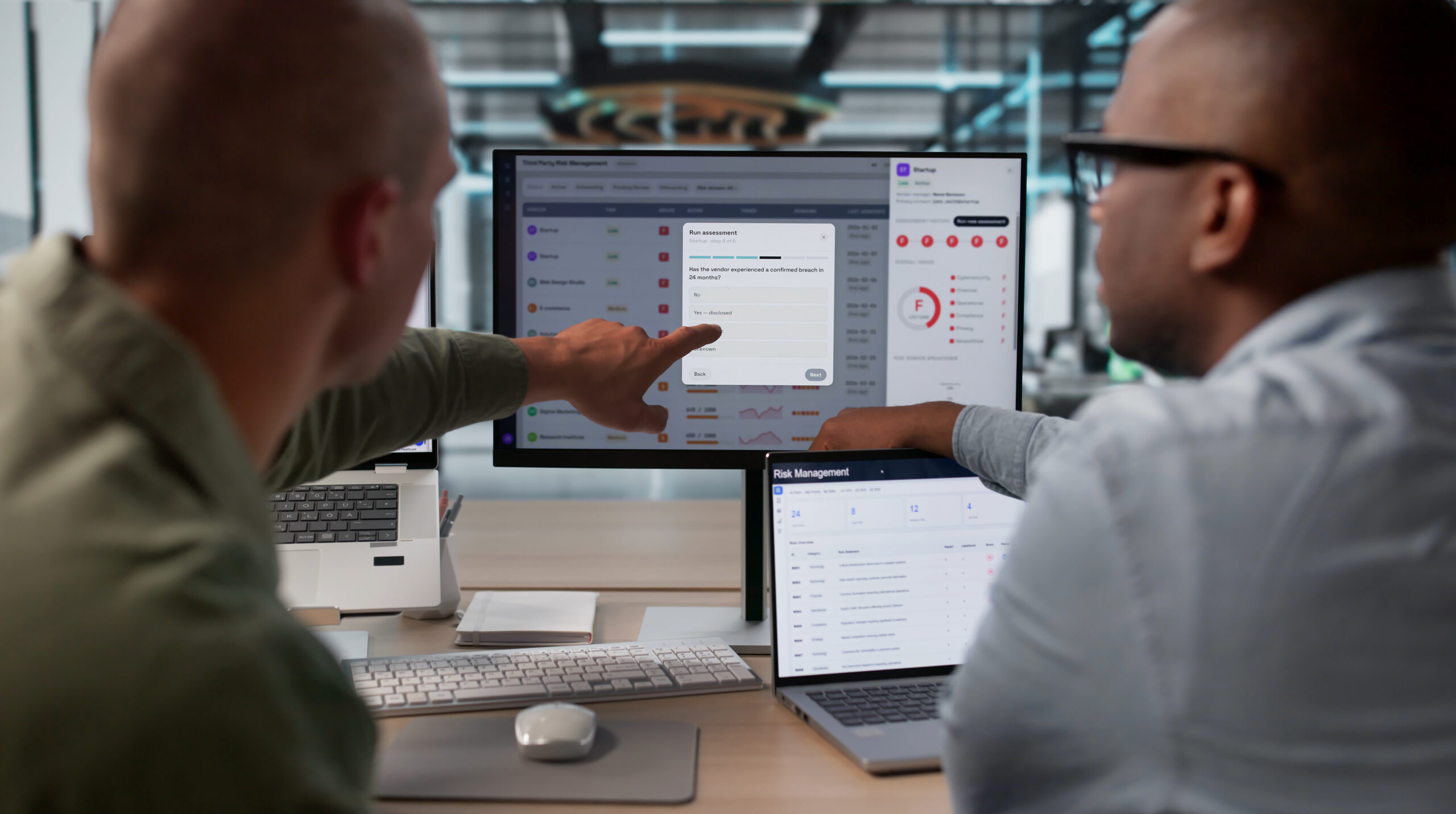 Two IT professionals reviewing computer screens in an office, collaborating on cybersecurity monitoring, identifying potential security threats and protecting business systems.